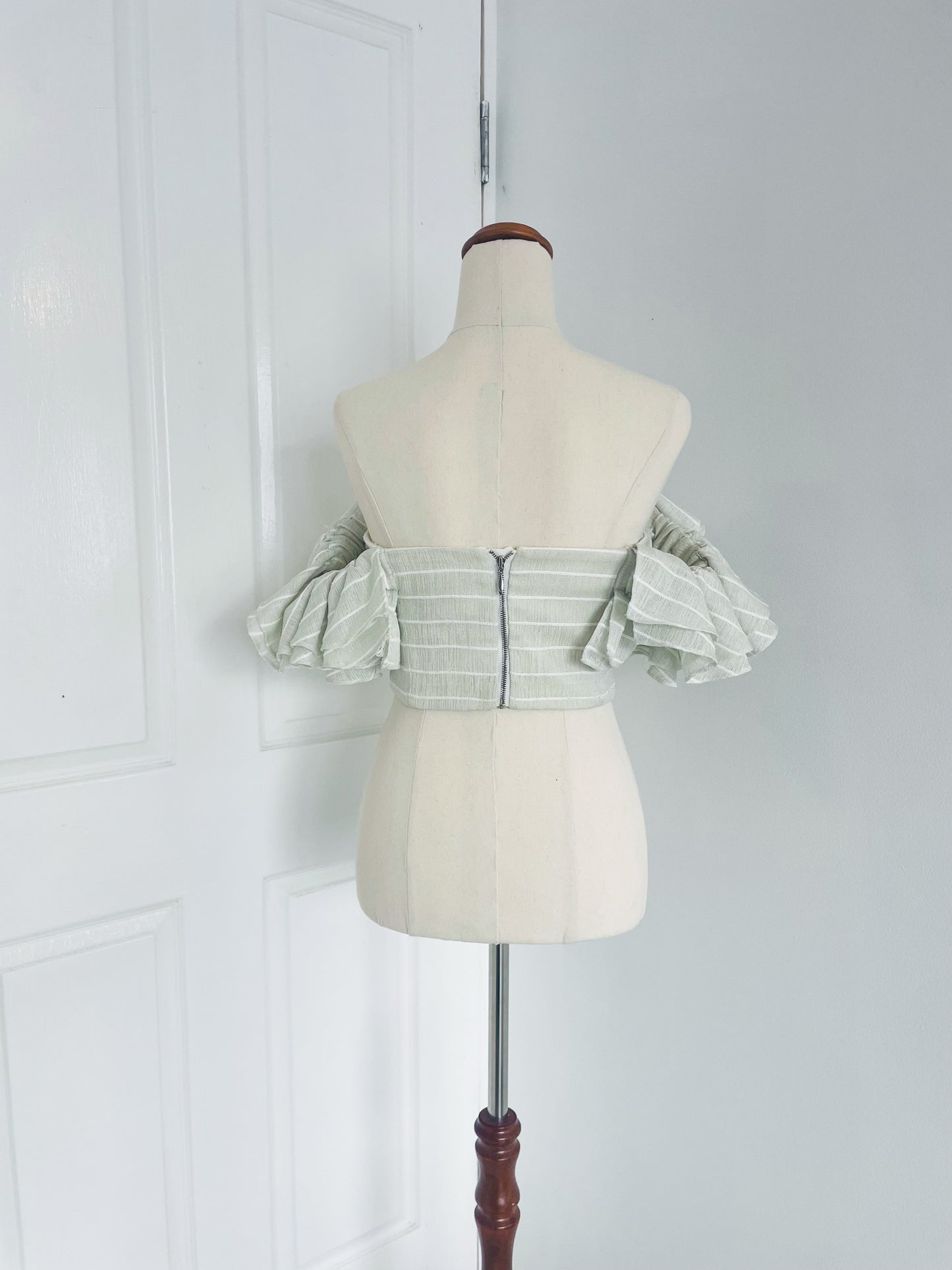 back view of a white mannequin displays a mint green, pinstripe , off the shoulder crop top with layered ruffles. designed by Acler. back zipper closure