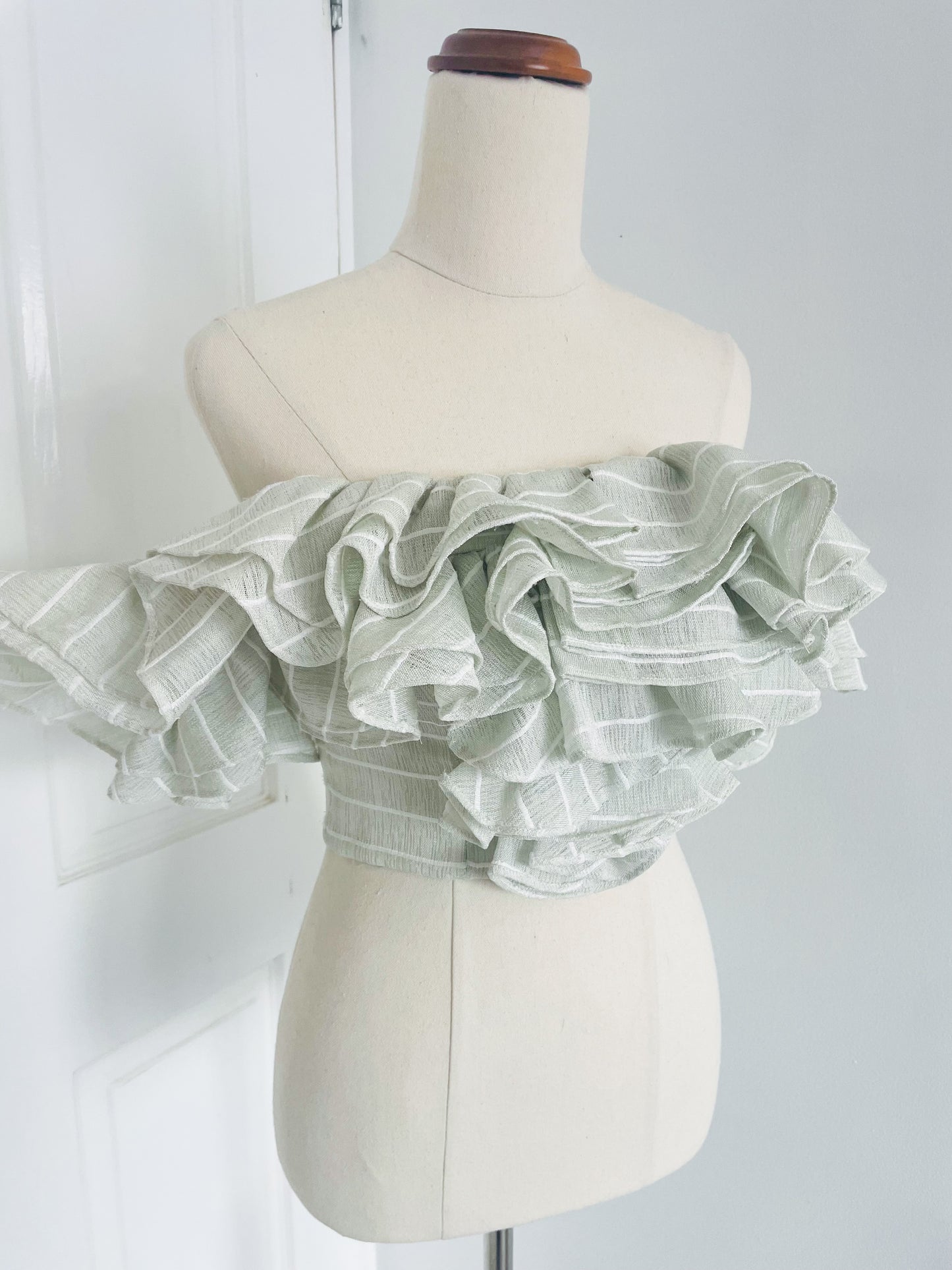 a white mannequin displays upclose of  a mint green, pinstripe , off the shoulder crop top with layered ruffles. designed by Acler. 