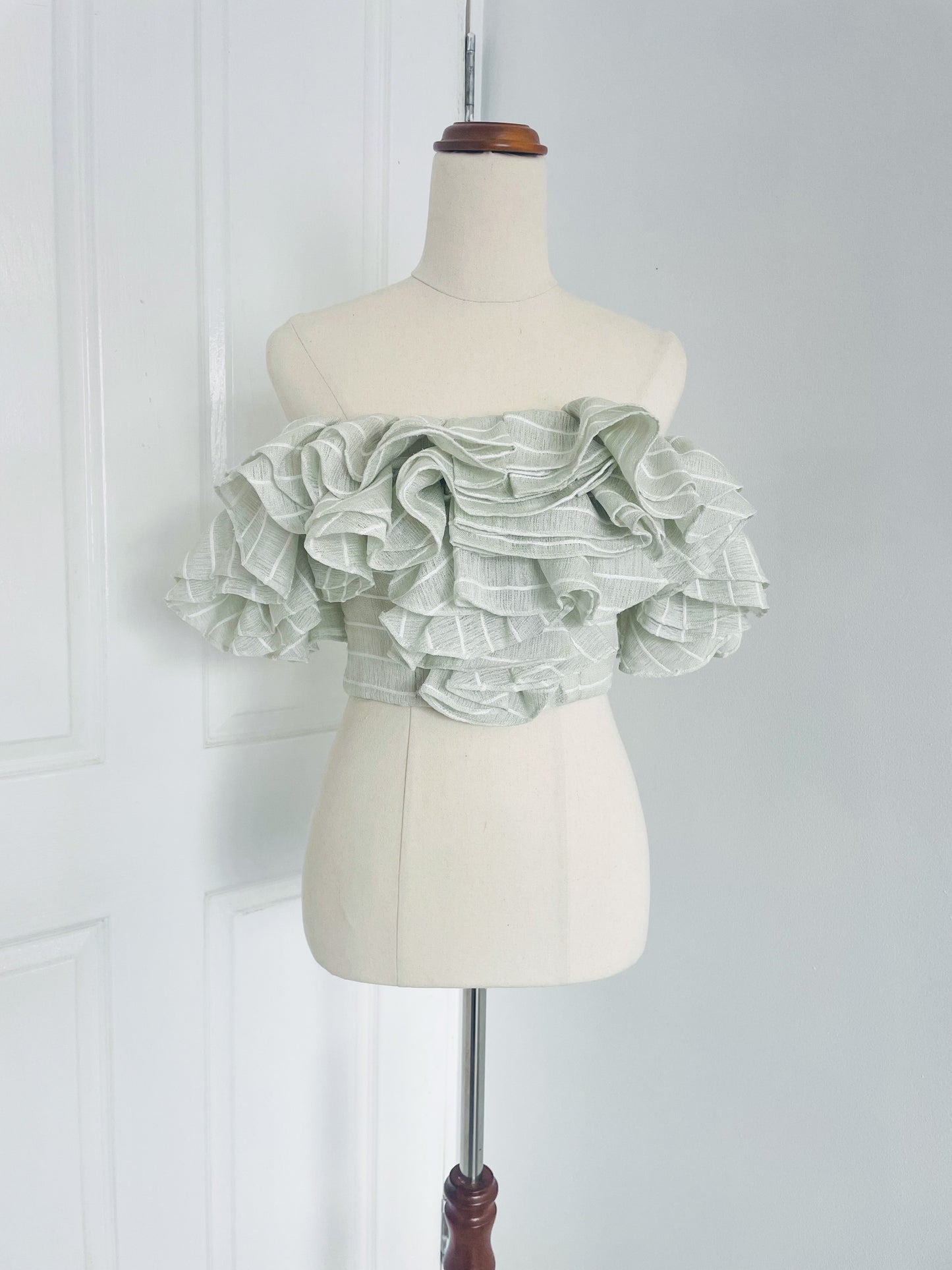 a white mannequin displays a mint green, pinstripe , off the shoulder crop top with layered ruffles. designed by Acler. 