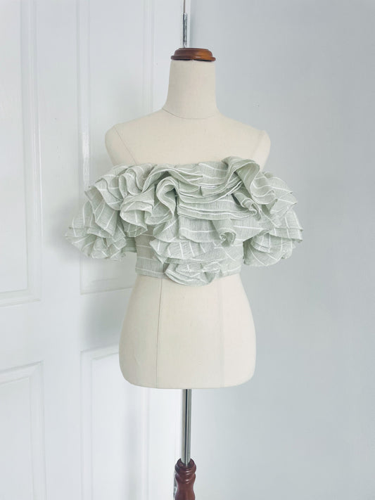 a white mannequin displays a mint green, pinstripe , off the shoulder crop top with layered ruffles. designed by Acler. 