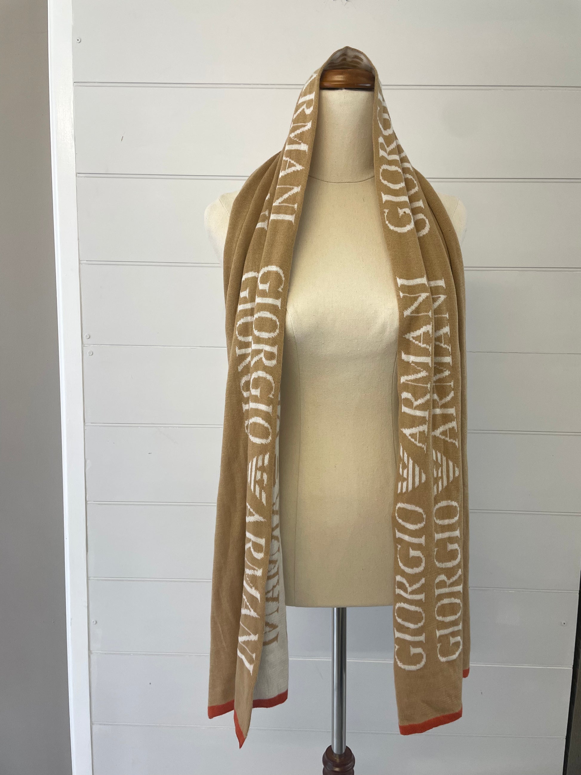 Giorgio Armani 100% wool scarf. Camel colour with white font and orange hem hanging on a mannequin